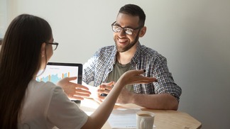 Two friendly businesspeople discussing contract details. Female agent explains contract, deal, loan details to smiling man. Coworkers negotiating, planning teamwork. Increasing charts on laptop screen