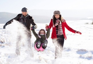Father and mother having fun with their daughter, playing in the snow. Sunny white winter nature.